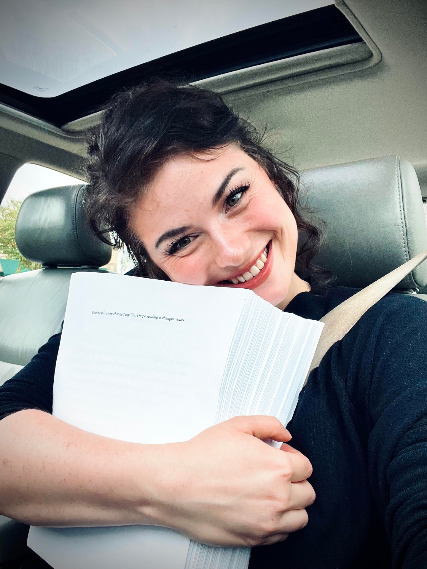 Madison smiling, hugging her finished manuscript in the car